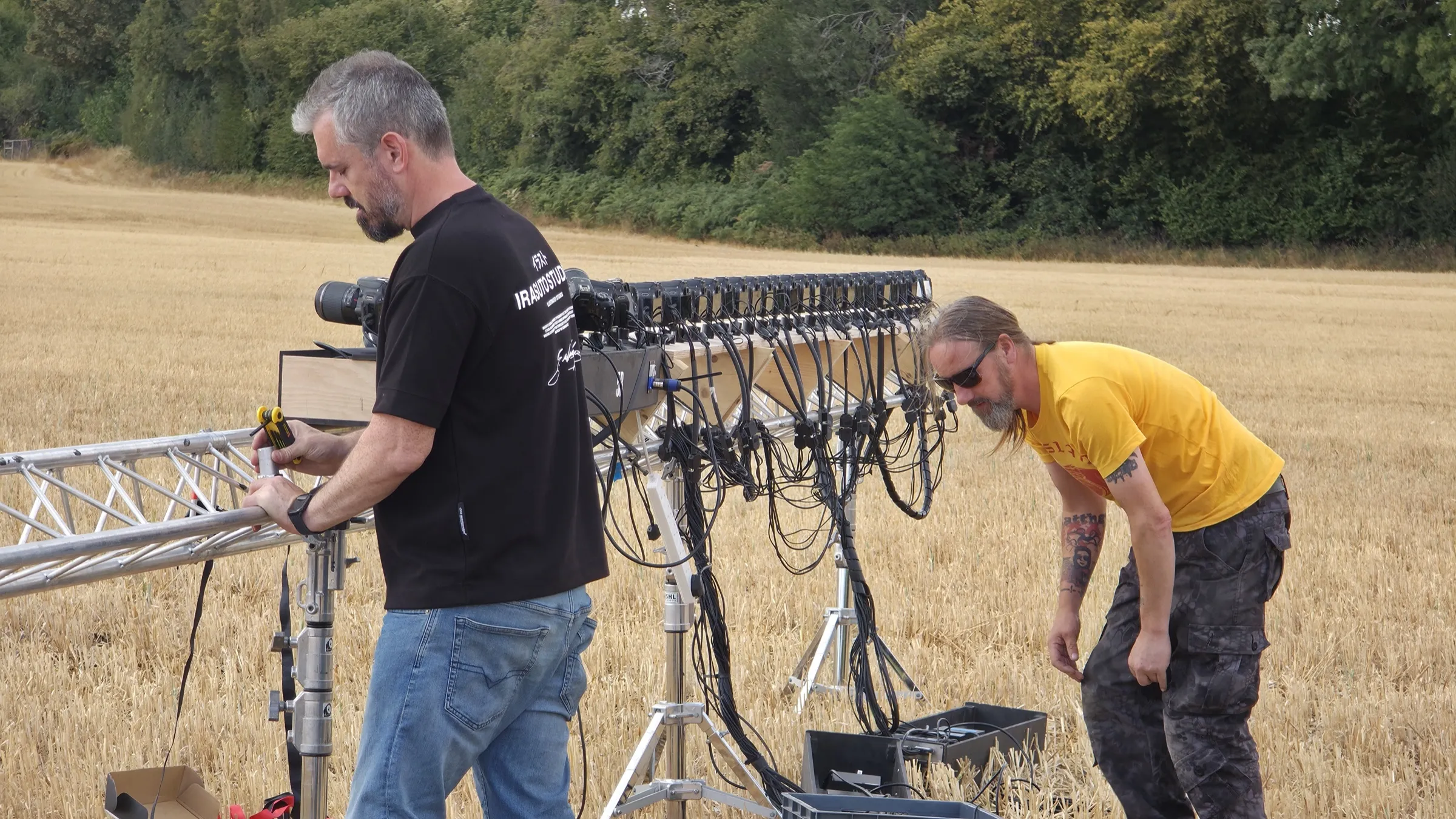 The straight line of stills cameras on a truss across a stubble field, with the crew van parked in front